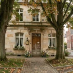 Façade d'une entreprise de pompes funèbres dans le Nord de la France, entourée d'arbres aux feuilles d'automne et d'arrangements floraux discrets